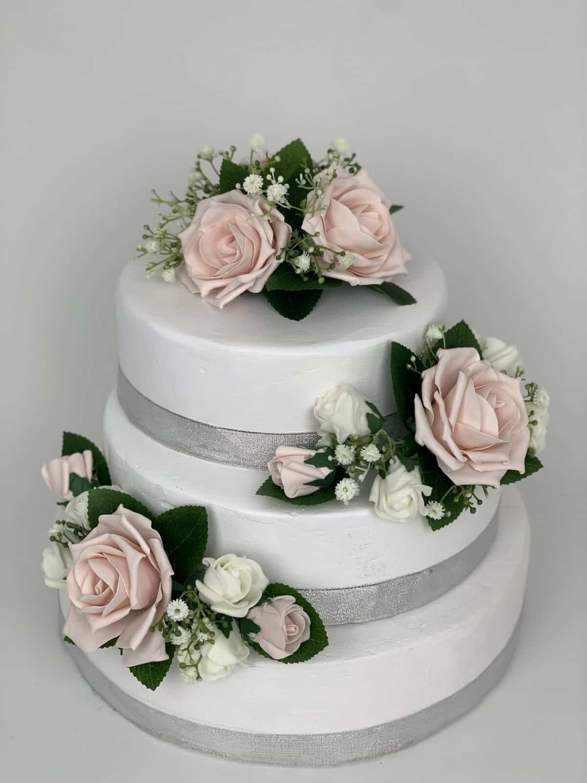 A simple 2-tiered wedding cake with pink ribbons and rose and peony topper