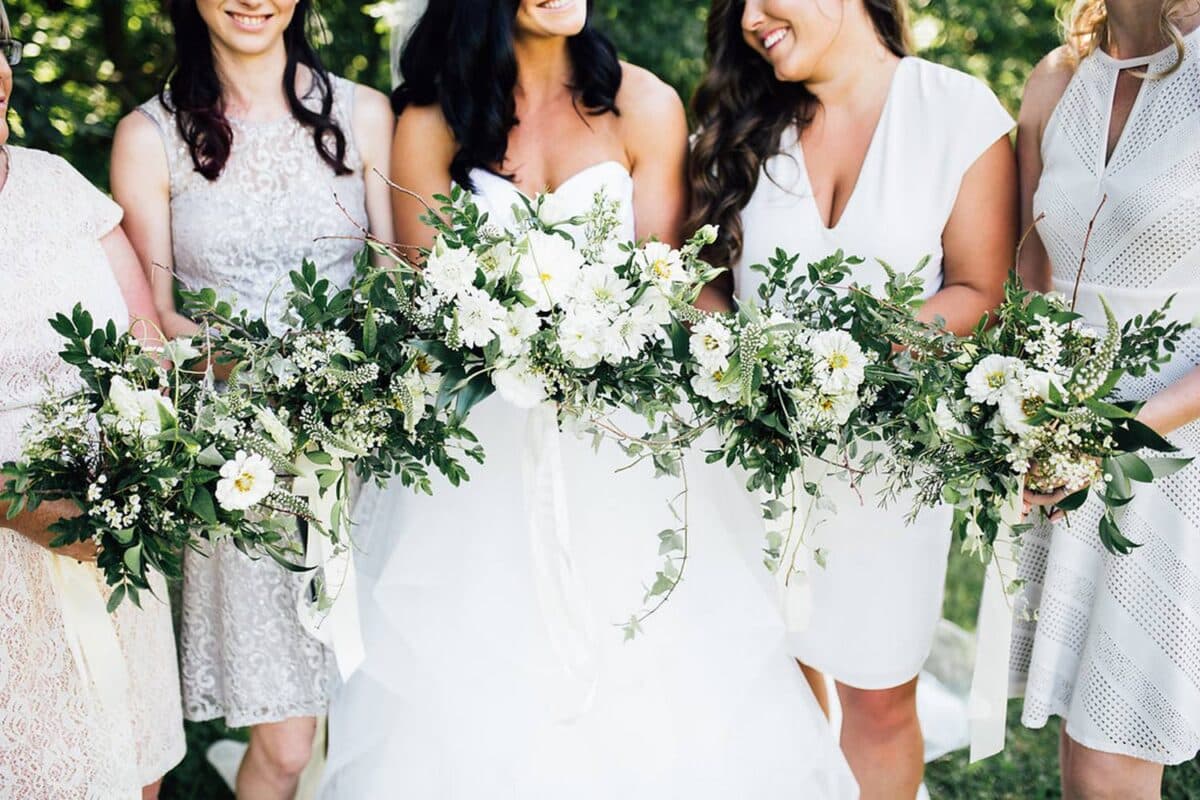 Beautiful Bride And Her Bridesmaids holding white floral and greenery bouquet